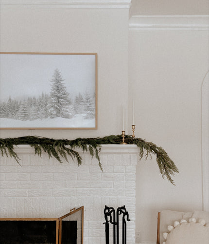 White fireplace with greenery and a framed landscape painting on the wall.
